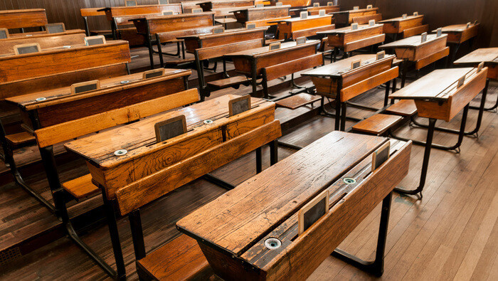 A Victorian-era classroom scene showing children seated at wooden desks, representing the strict and disciplined schooling of the nineteenth century