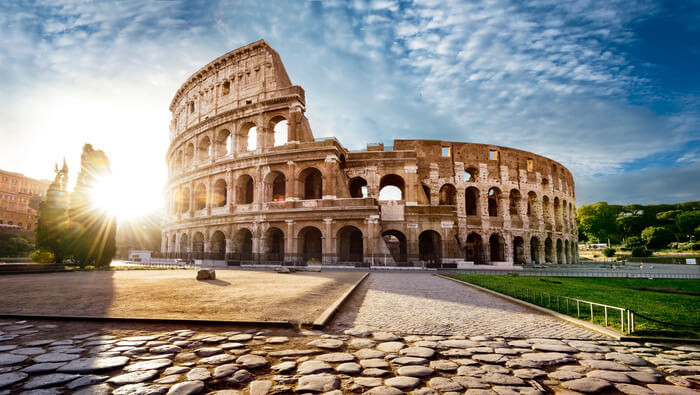 Child-friendly illustration of Ancient Roman architecture featuring the Colosseum, aqueducts, marble temples with columns, and Roman buildings welcoming young explorers