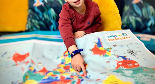 Child pointing at a colourful Mysteries in Time world map from a Christmas gift box